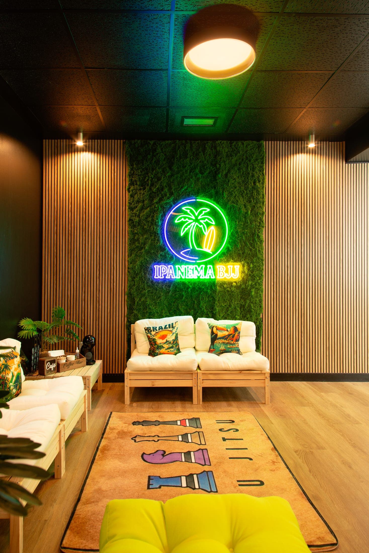 Zona de recepción y lounge de Ipanema BJJ Gijón, con el neón de la palmera